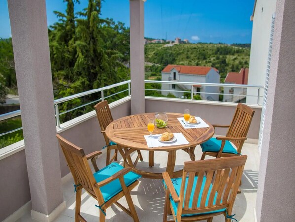 Enjoy meals on the balcony with a view of the lush landscape, surrounded by a round table and comfortable seating for four.