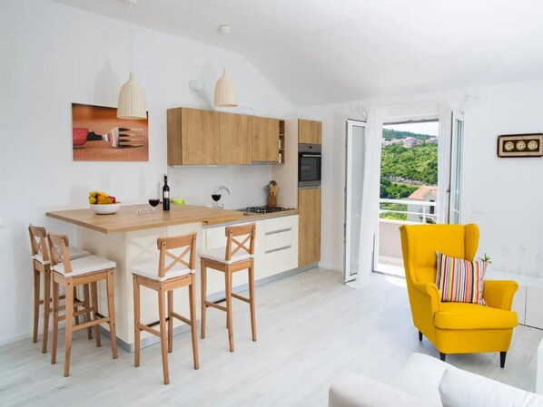 A modern kitchen with wooden cabinets, a central island with bar stools, and a yellow armchair.