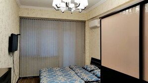 Ein Schlafzimmer mit einem Bett, einem Deckenventilator, einem an der Wand montierten Fernseher und einem Fenster mit Jalousien.