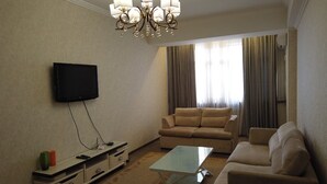 Ein Wohnzimmer mit Flachbildfernseher, einer Couch, einem Couchtisch und einer Deckenleuchte.