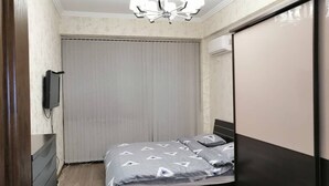 Ein Schlafzimmer mit einem Bett, einem Fernseher, einer Deckenleuchte und einer Schiebetür.