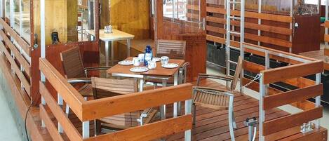 A wooden deck with tables and chairs, a small table with a few items, and a ladder.