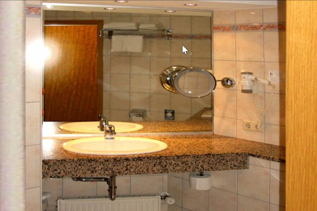 A bathroom with two sinks, a mirror, a towel rack, and a toilet paper dispenser.