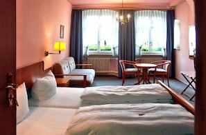 A hotel room with two beds, a sofa, a dining table with chairs, a lamp, and a window with curtains. - Gasthof Goldener Adler (Weissenburg in Bayern)