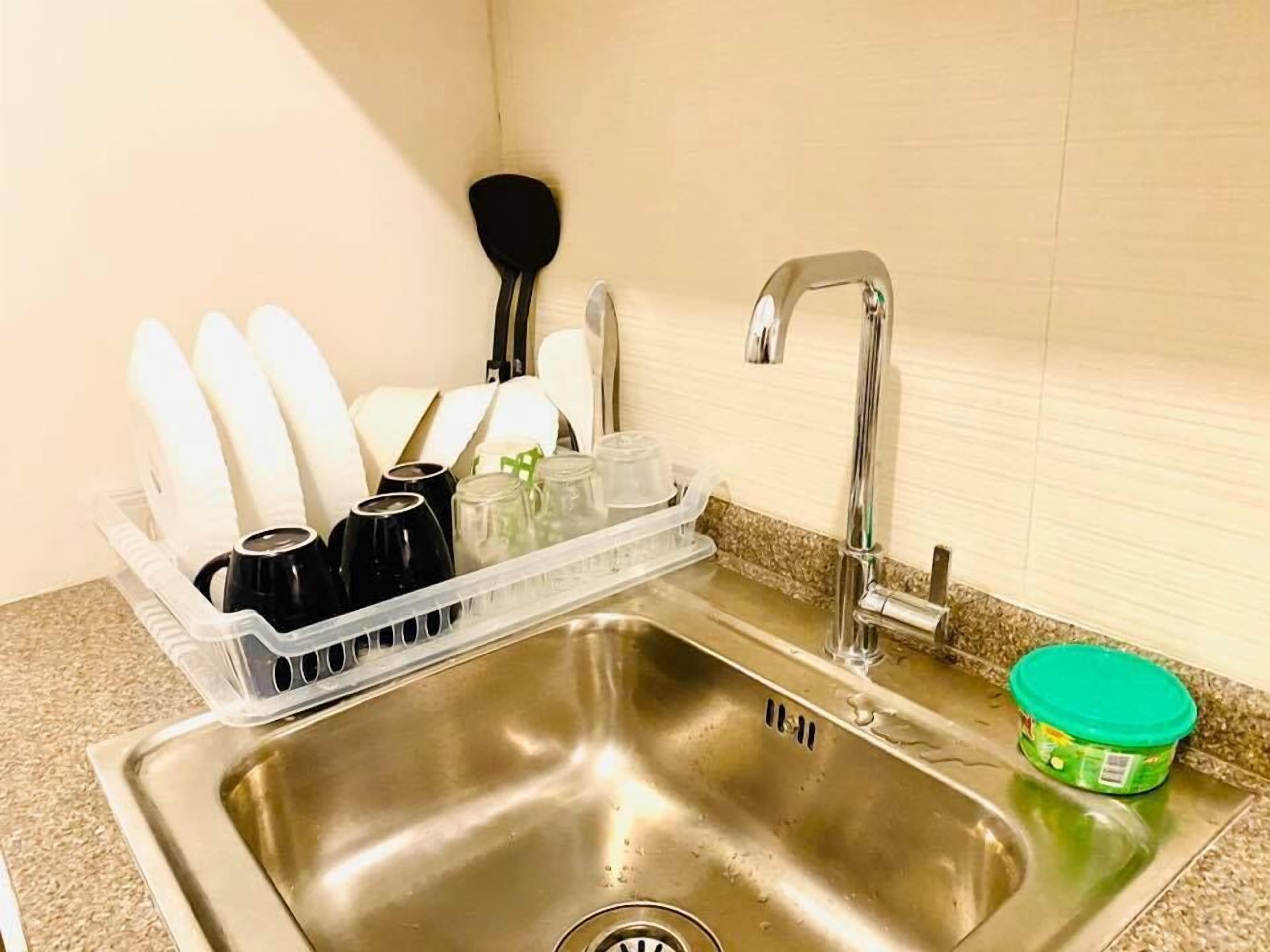A stainless steel kitchen sink with a dish rack holding cups and a green container.