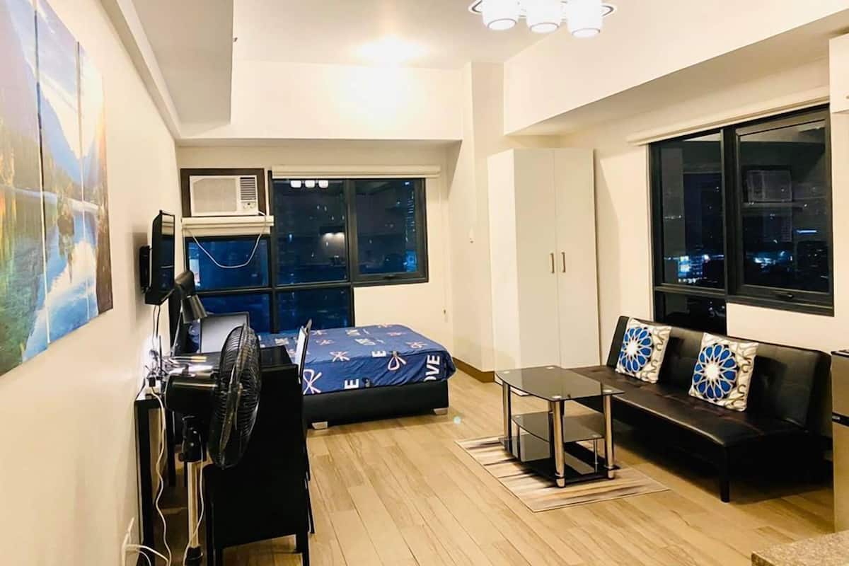 A modern room with a bed, a desk with a computer, a sofa, and a window with a city view.