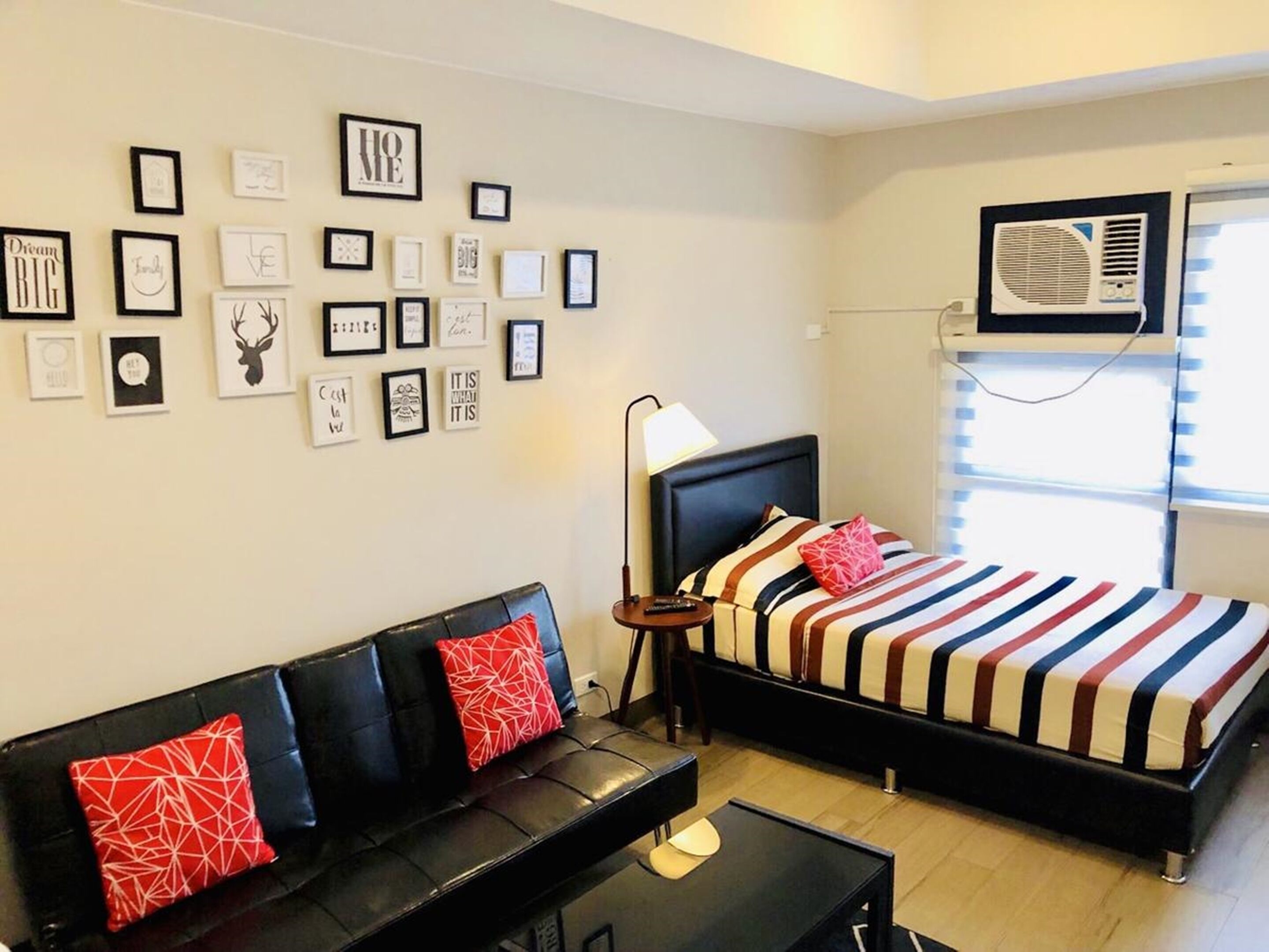 Un dormitorio con cama, un sofá negro, una mesita y una pared decorada con cuadros.