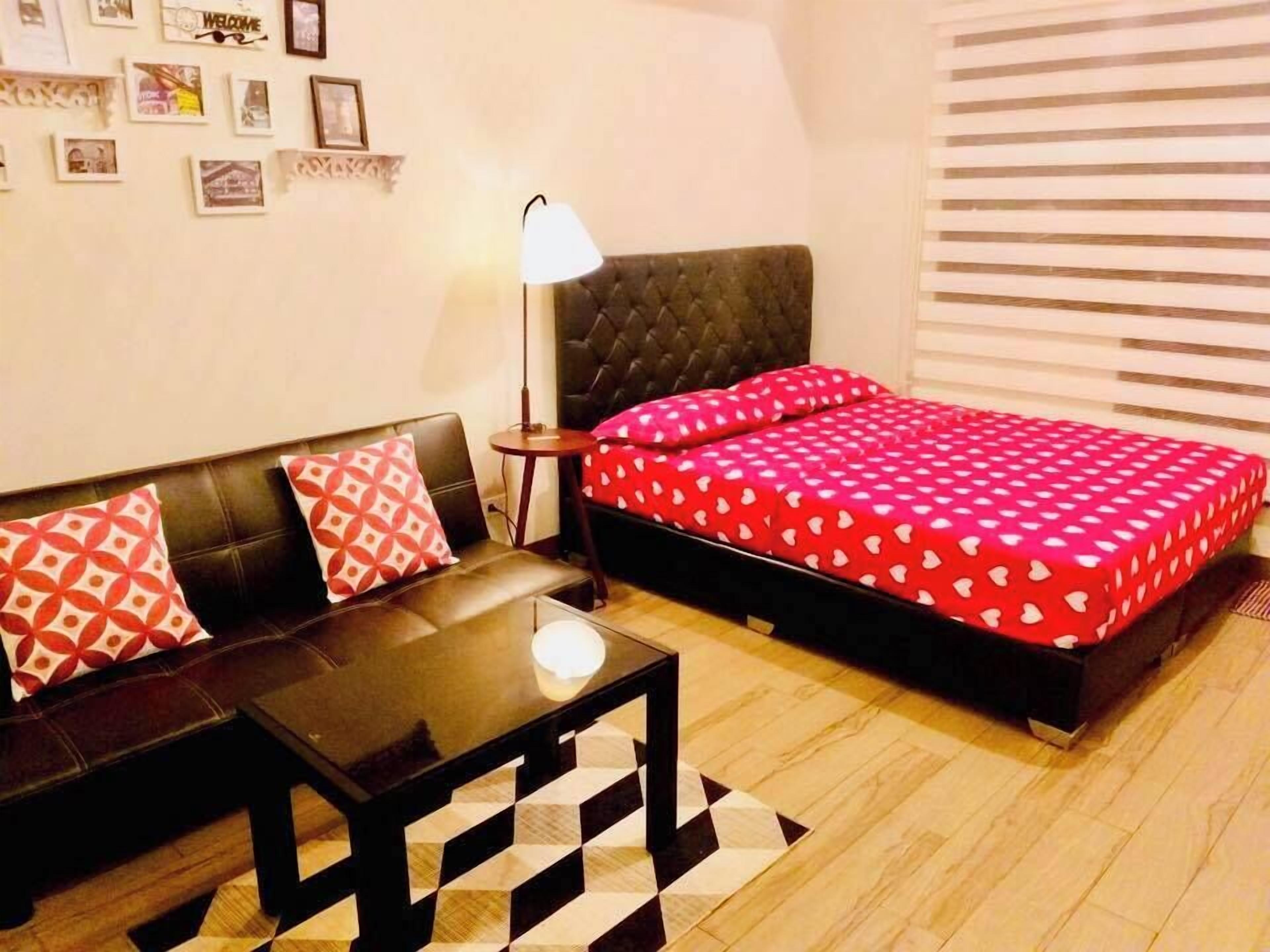 A room with a bed, a sofa, a small table, and a lamp.