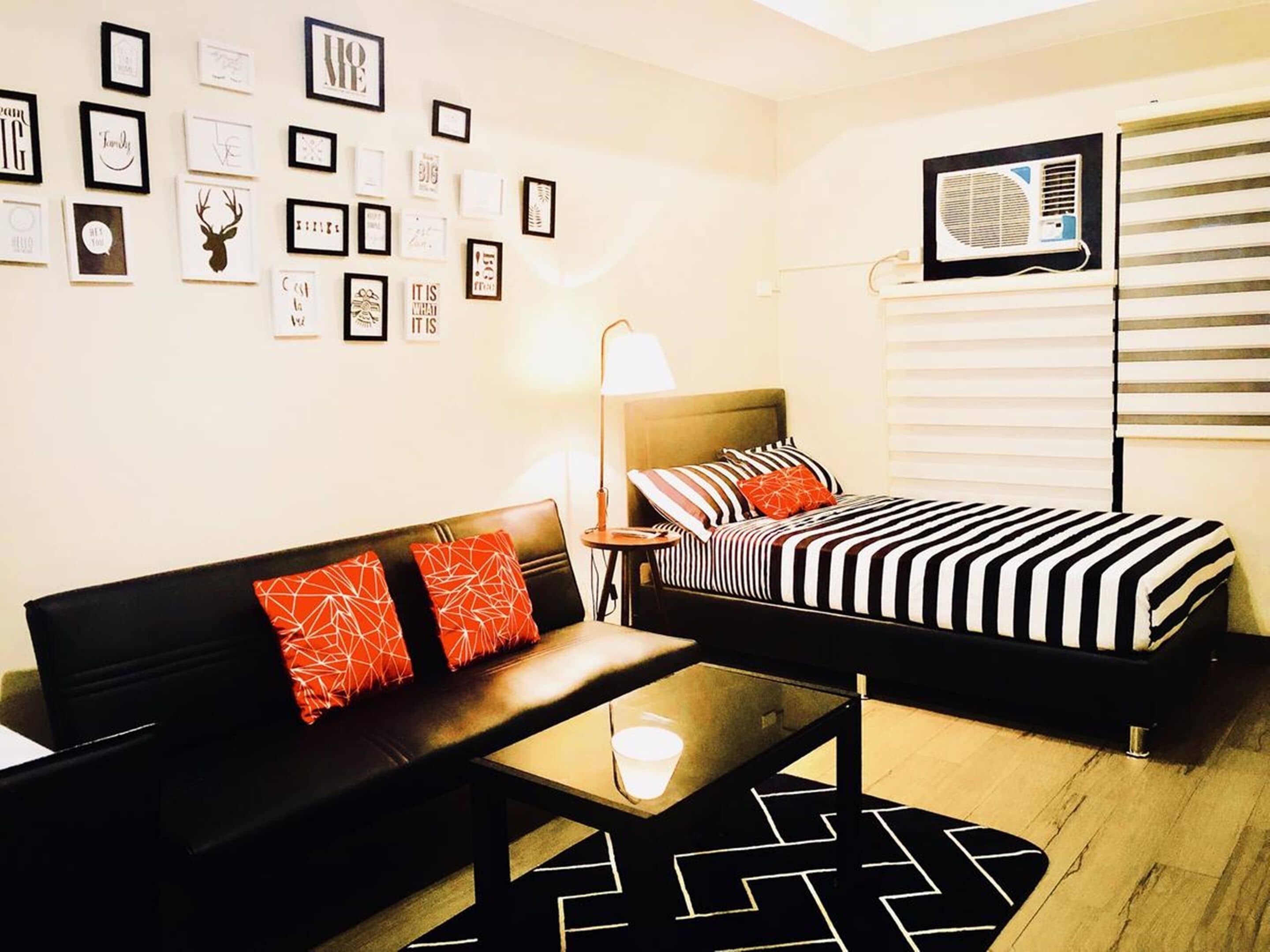 A compact hotel room with a bed, a sofa, a small table, and a wall adorned with framed pictures.
