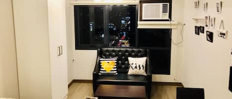 Un espacio habitable compacto con un sofá de cuero negro, una mesita y una ventana con vistas a la ciudad.