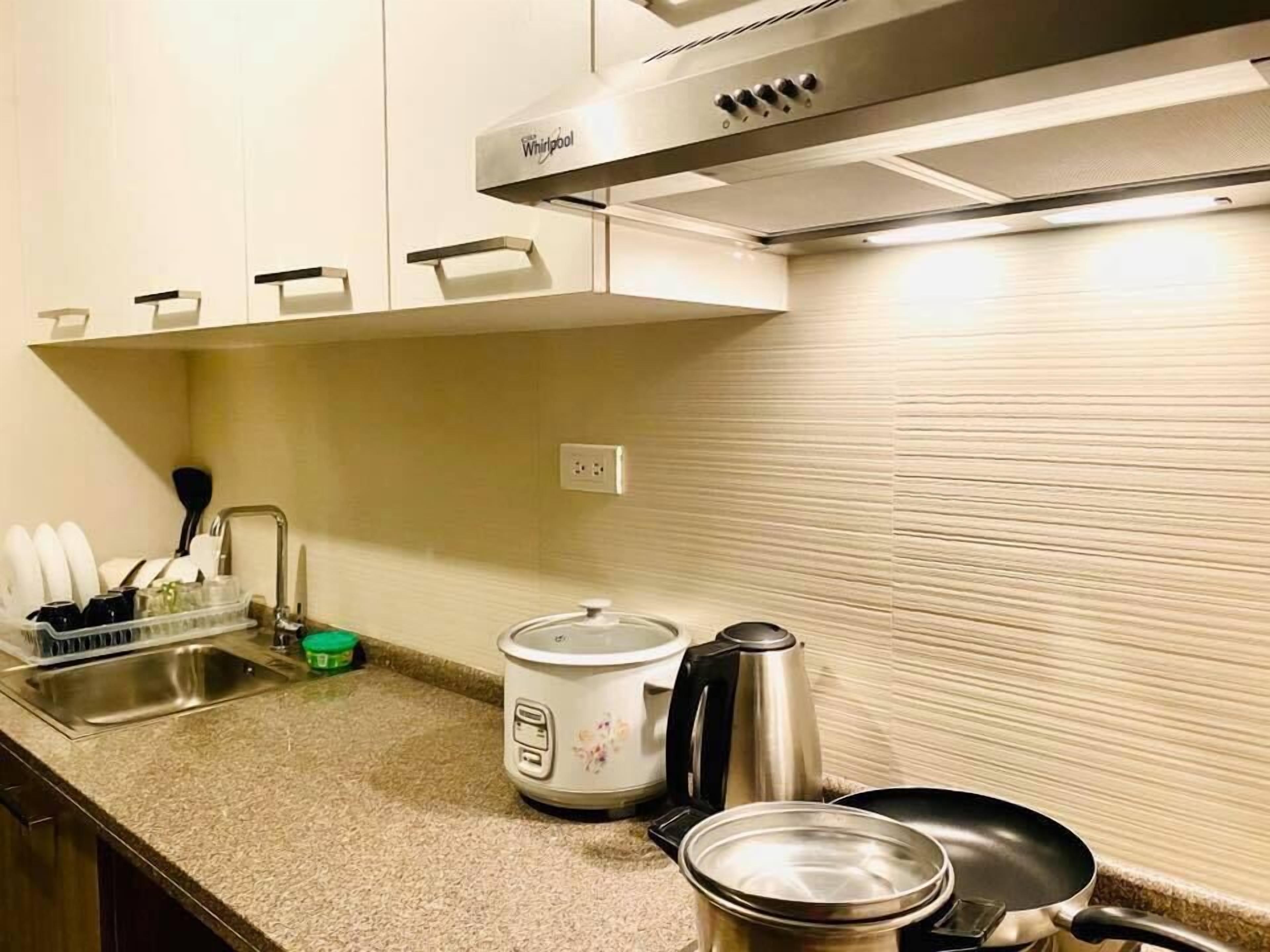 A kitchen with a stainless steel range hood, a sink, a kettle, a frying pan, and a slow cooker.