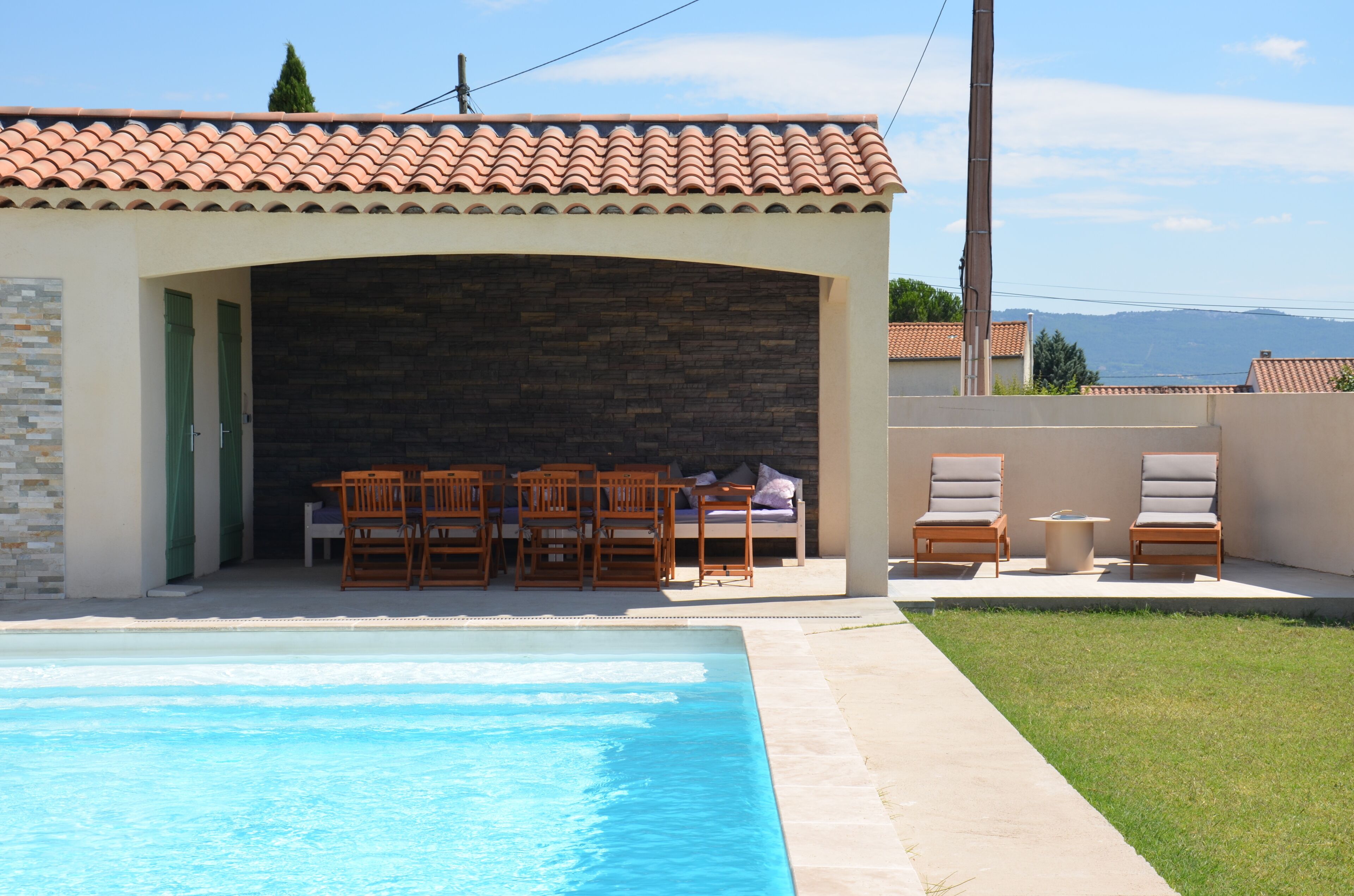 A poolside area with a covered seating area, a stone wall, and a view of the mountains.