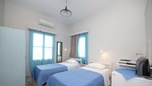 A hotel room with two beds, a desk with a computer, and an air conditioning unit. - Twin Shades (Kalymnos)