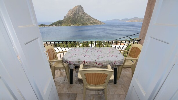 A balcony with a table and four chairs, overlooking a coastal view with a prominent rock formation. - Twin Shades (Kalymnos)