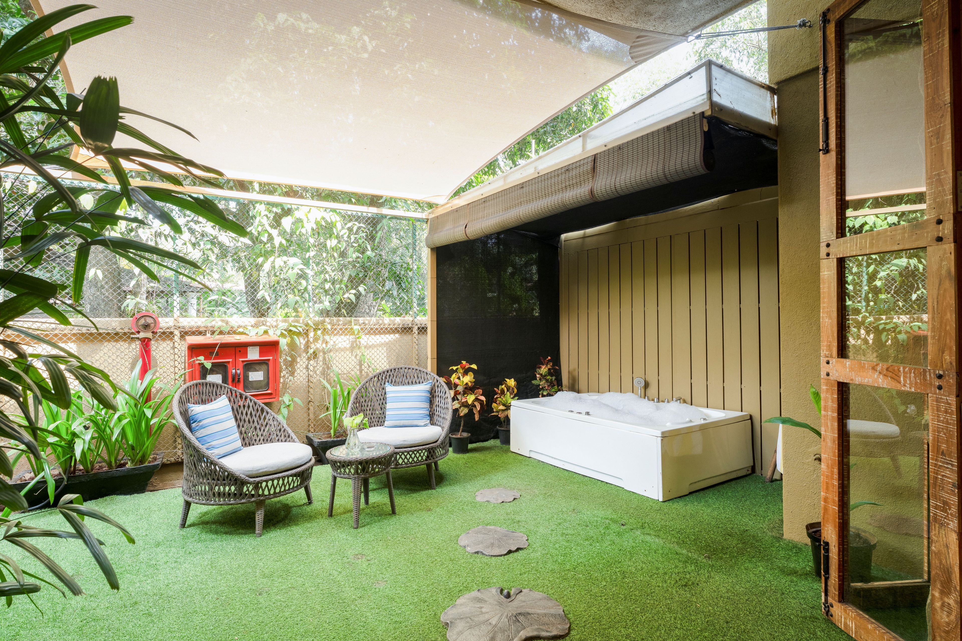 A covered outdoor seating area with artificial grass, wicker chairs, a white sofa, and a red utility cabinet.