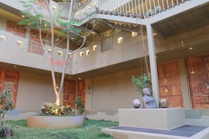 A multi-level atrium with a central garden, wooden doors, and a hanging plant. - 3102bce A Vedic Resort (Vagator)