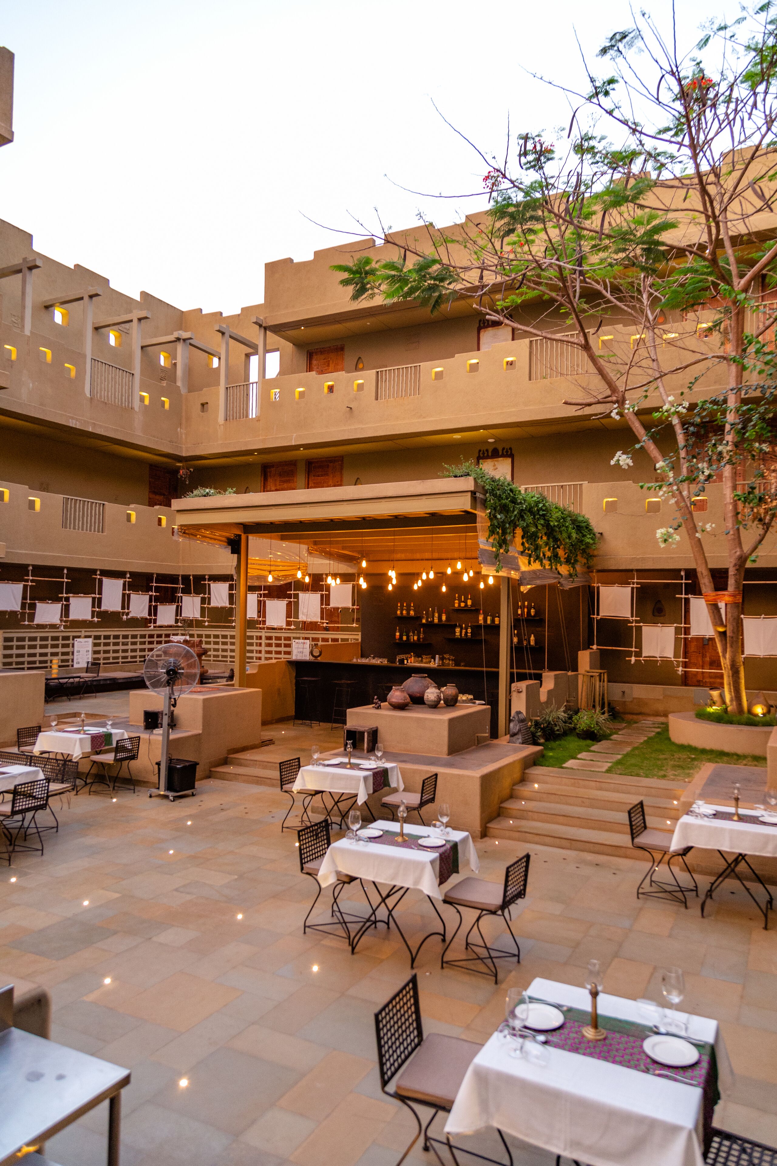 An outdoor dining area with multiple tables and chairs, a bar area, and a staircase leading to an upper level.