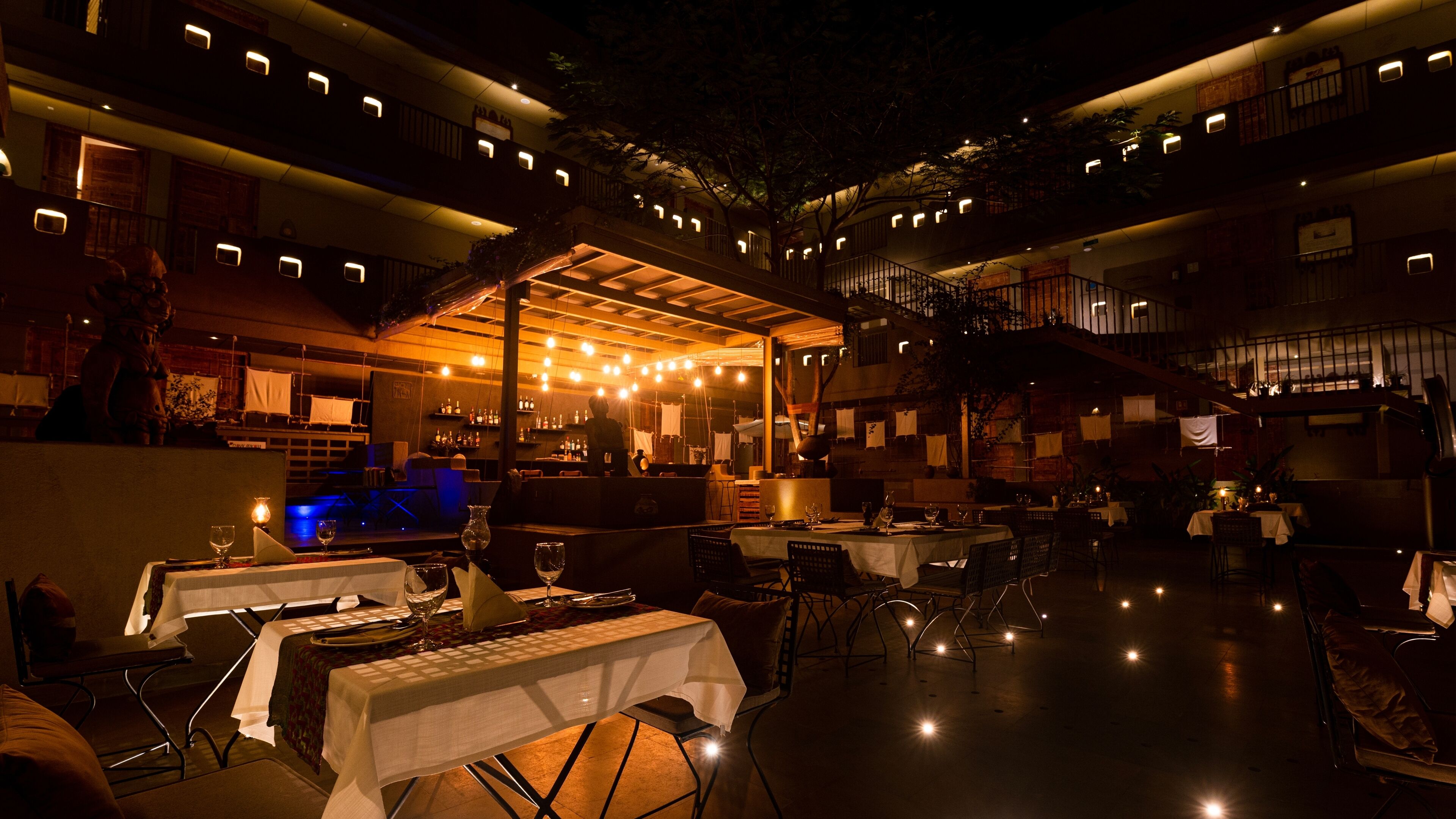 An outdoor dining area with tables and chairs, a bar, and a staircase leading to an upper level.