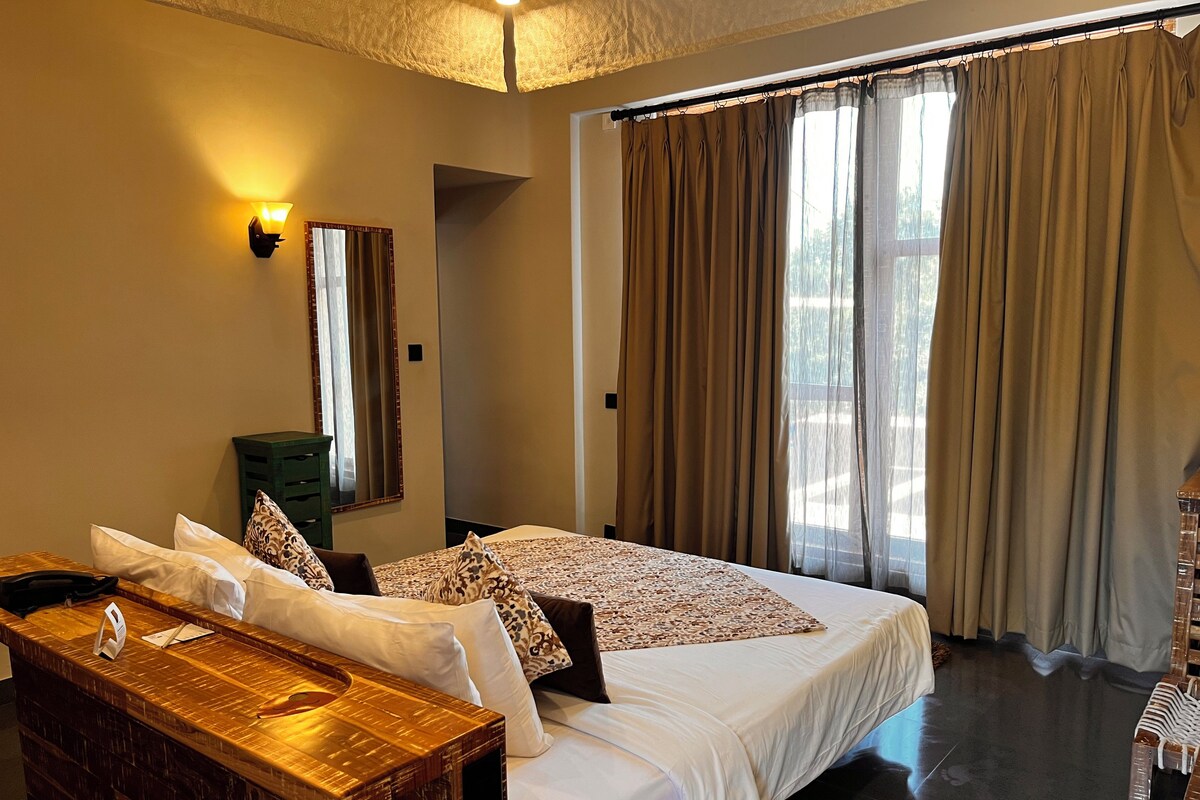 A hotel room with a large bed, a wooden desk, a mirror, and a window with curtains.