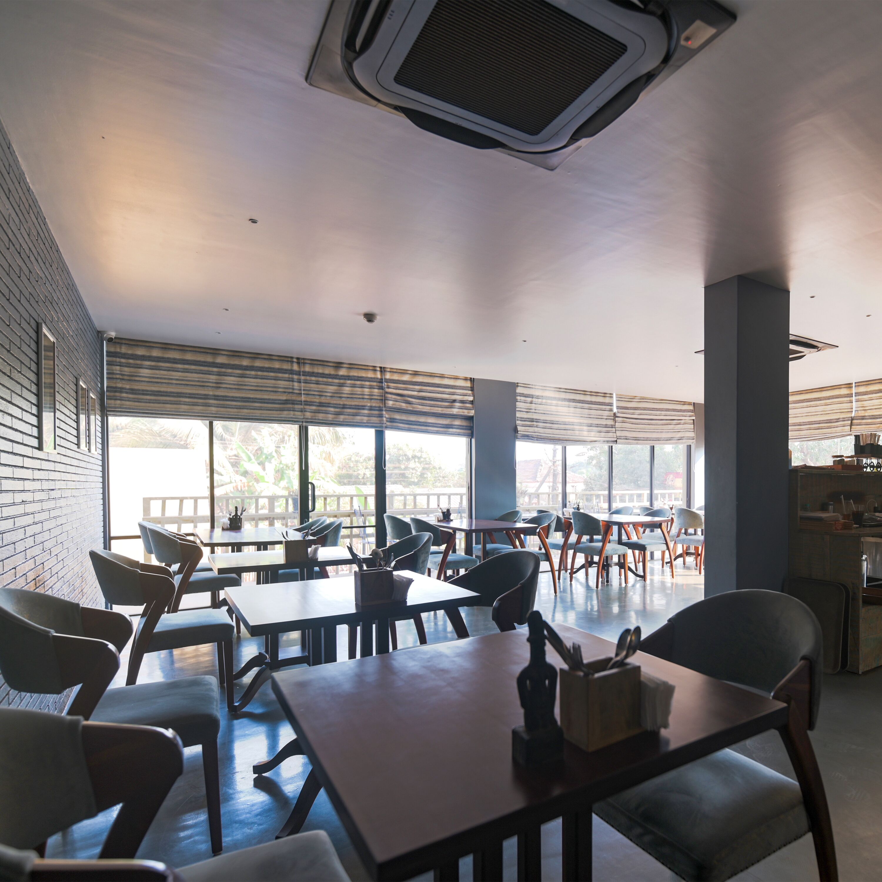A modern dining area with tables and chairs, large windows, and a brick wall.