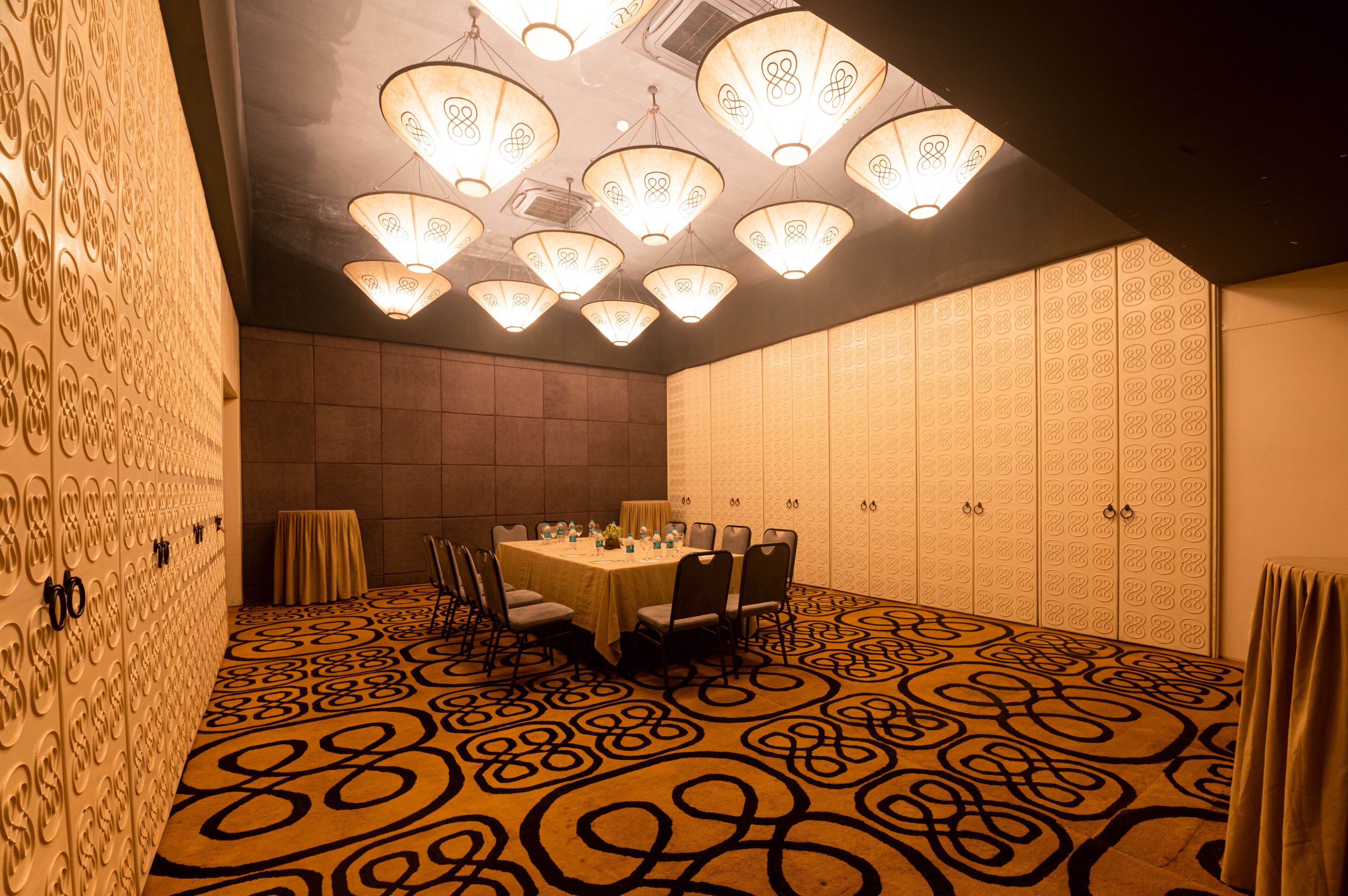 A conference room with a patterned carpet, a round table with chairs, and decorative ceiling lights.