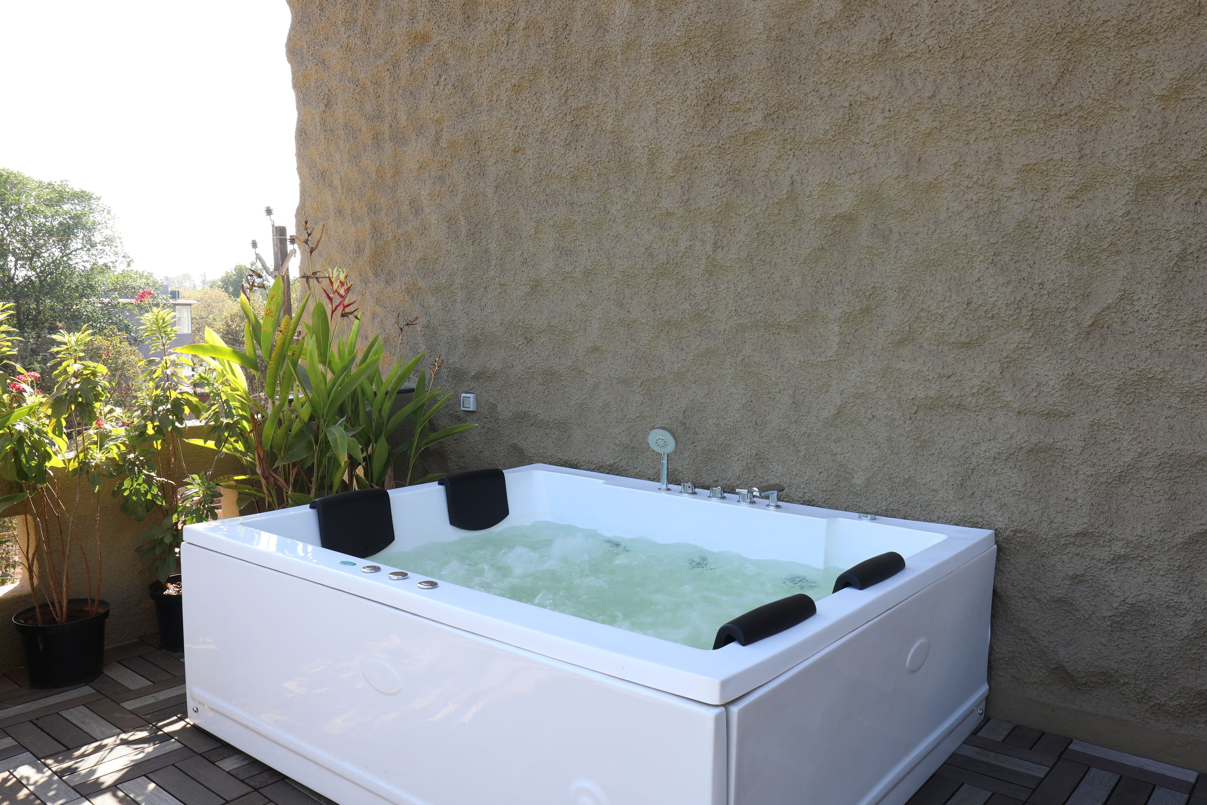 Un jacuzzi extérieur blanc, doté de jets, entouré de plantes en pot et adossé à un mur à texture.
