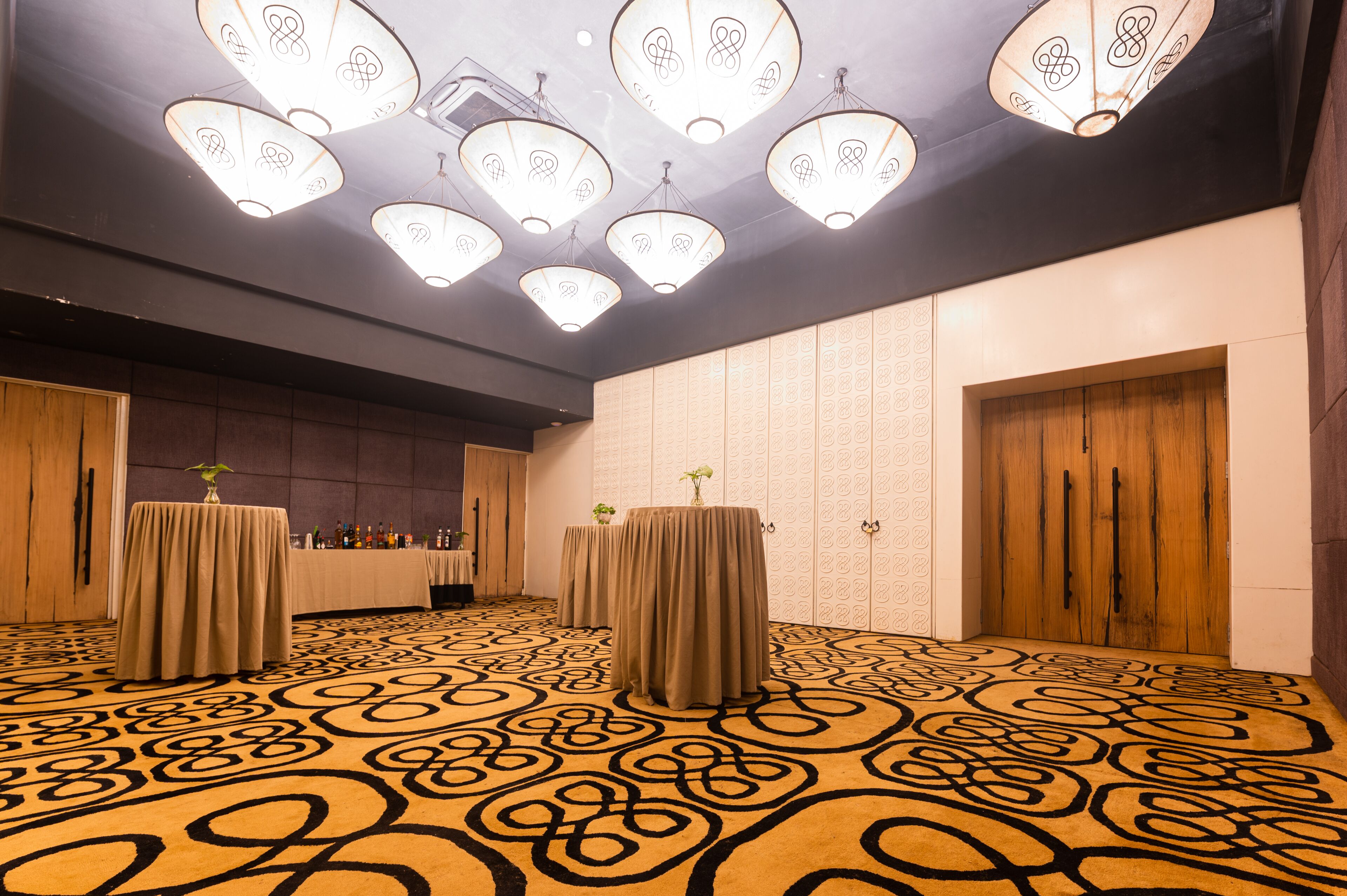 Un salón de conferencias con alfombra estampada, mesas cubiertas con manteles y lámparas colgantes.