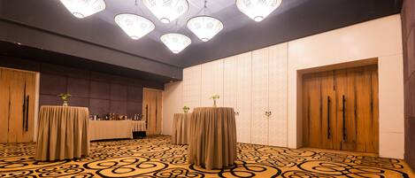 Un salón de conferencias con alfombra estampada, mesas cubiertas con manteles y lámparas colgantes.