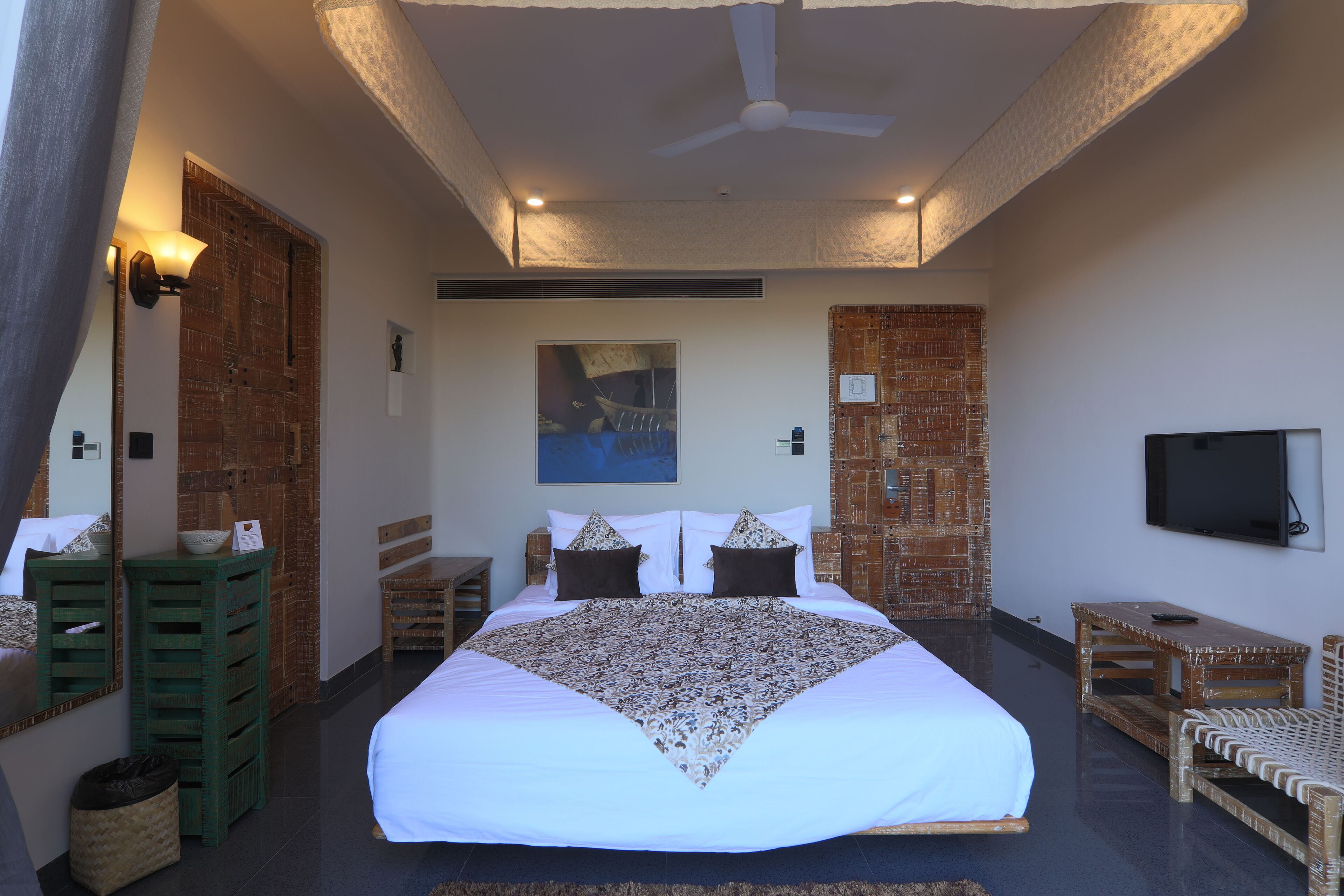 Ruime slaapkamer met een groot bed, een plafondventilator, een flatscreen televisie, rieten meubels en een groot raam.