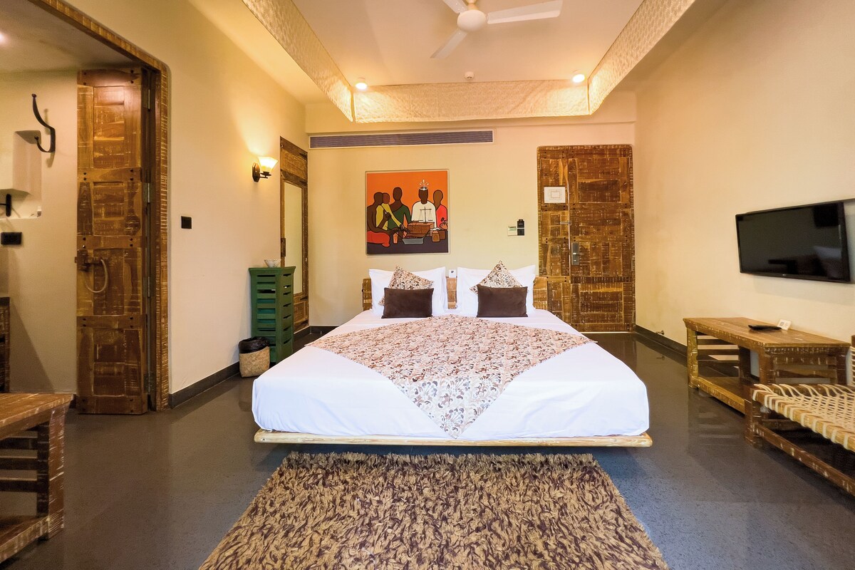 A spacious bedroom with a large bed, a flat-screen TV, a wooden bench, and a patterned rug.