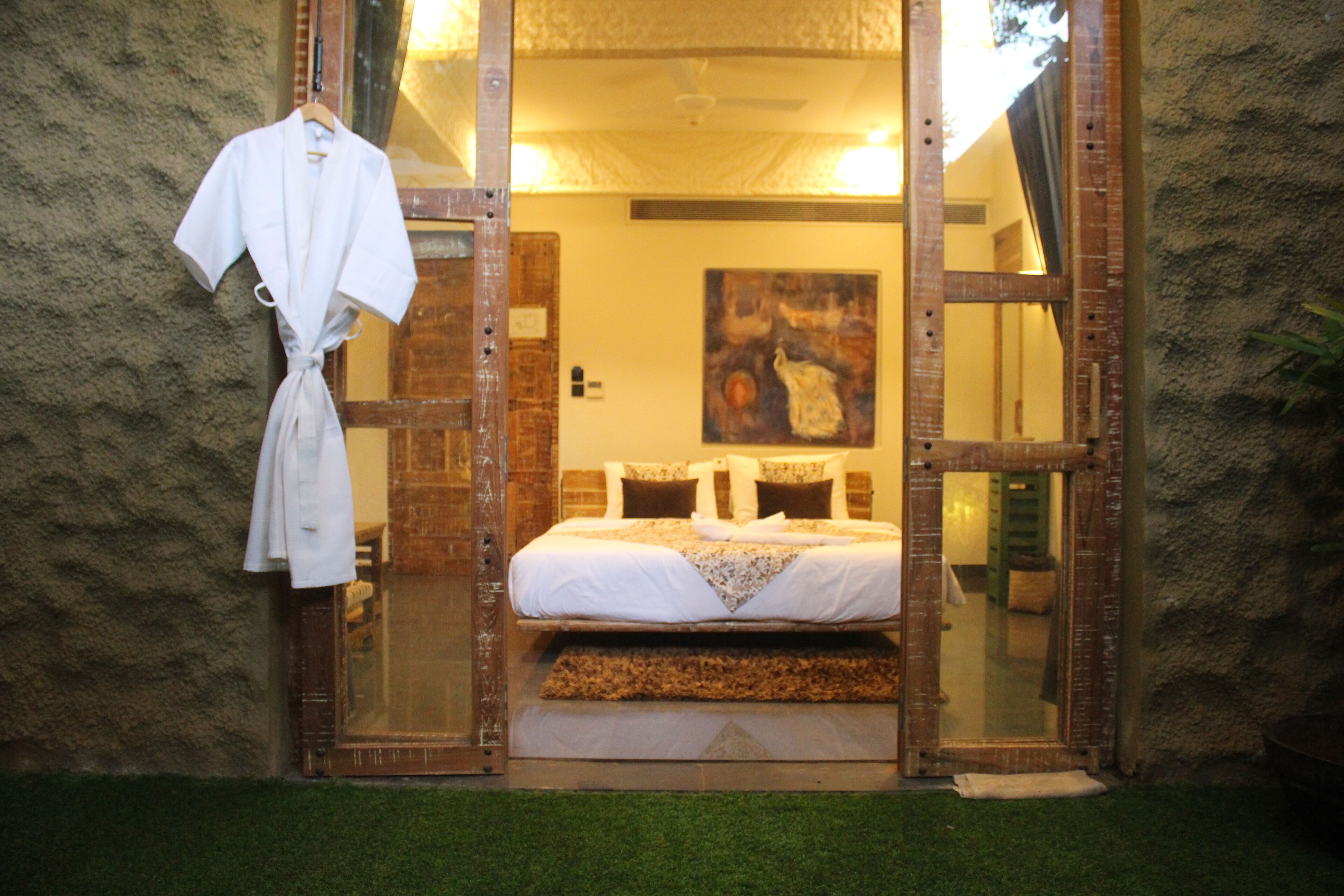 A bedroom with a bed, a painting on the wall, and a robe hanging on a hook.