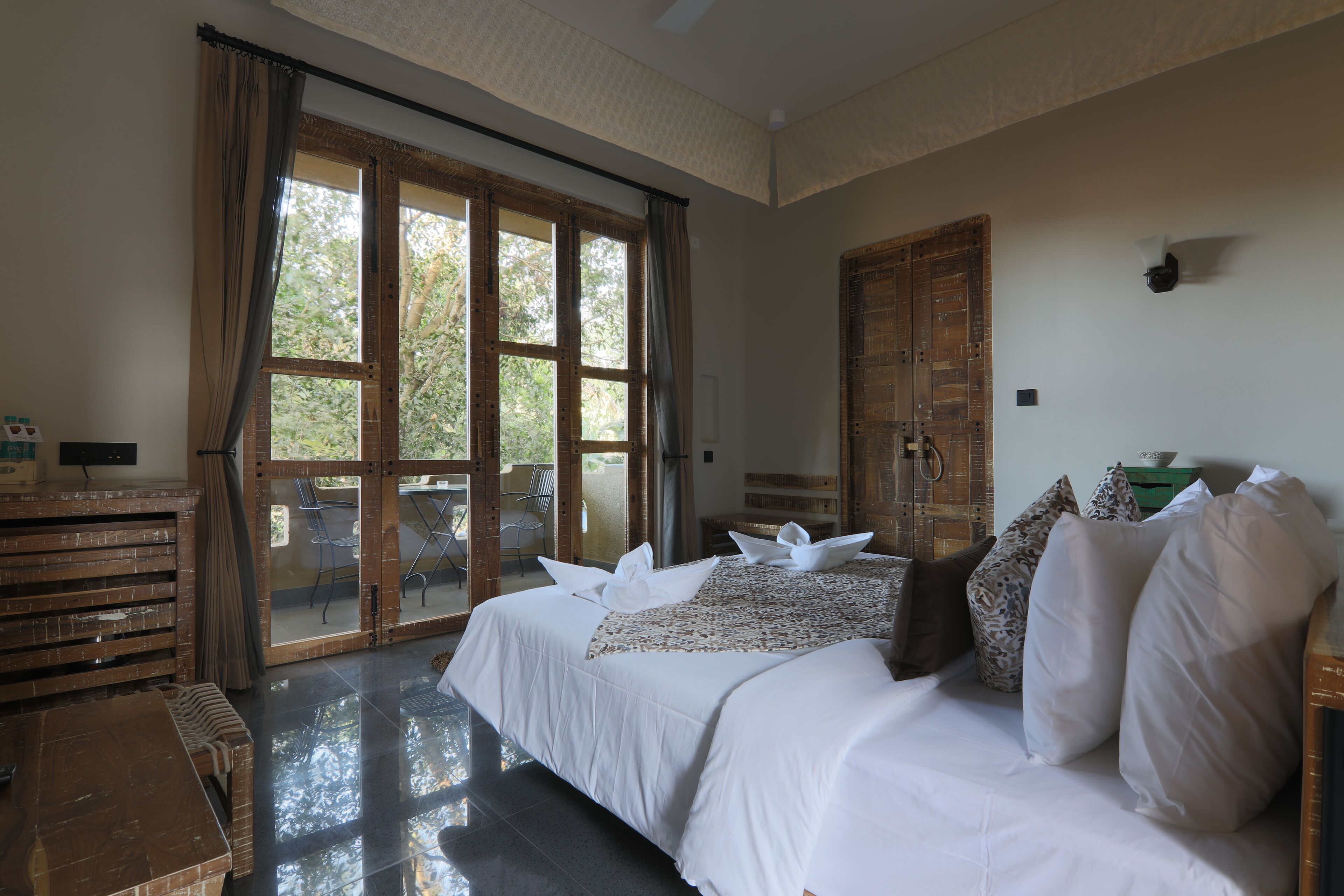Une chambre avec un grand lit, un banc en bois, une table et une vue sur l’extérieur grâce à une porte vitrée.