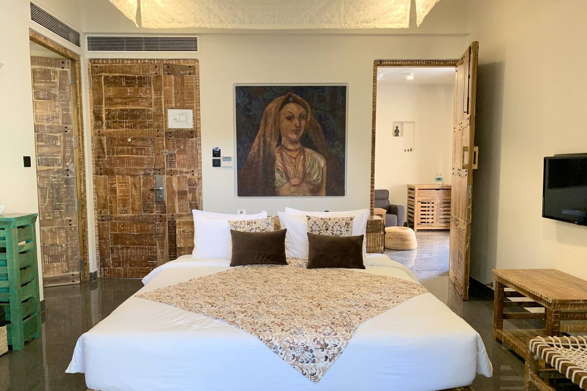 Una cama grande con un edredón estampado, un cuadro sobre ella y una puerta de madera con un diseño texturizado.