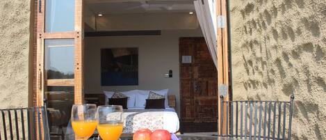 A glass table with two orange drinks, a plate with two apples, and a bed with pillows in the background.