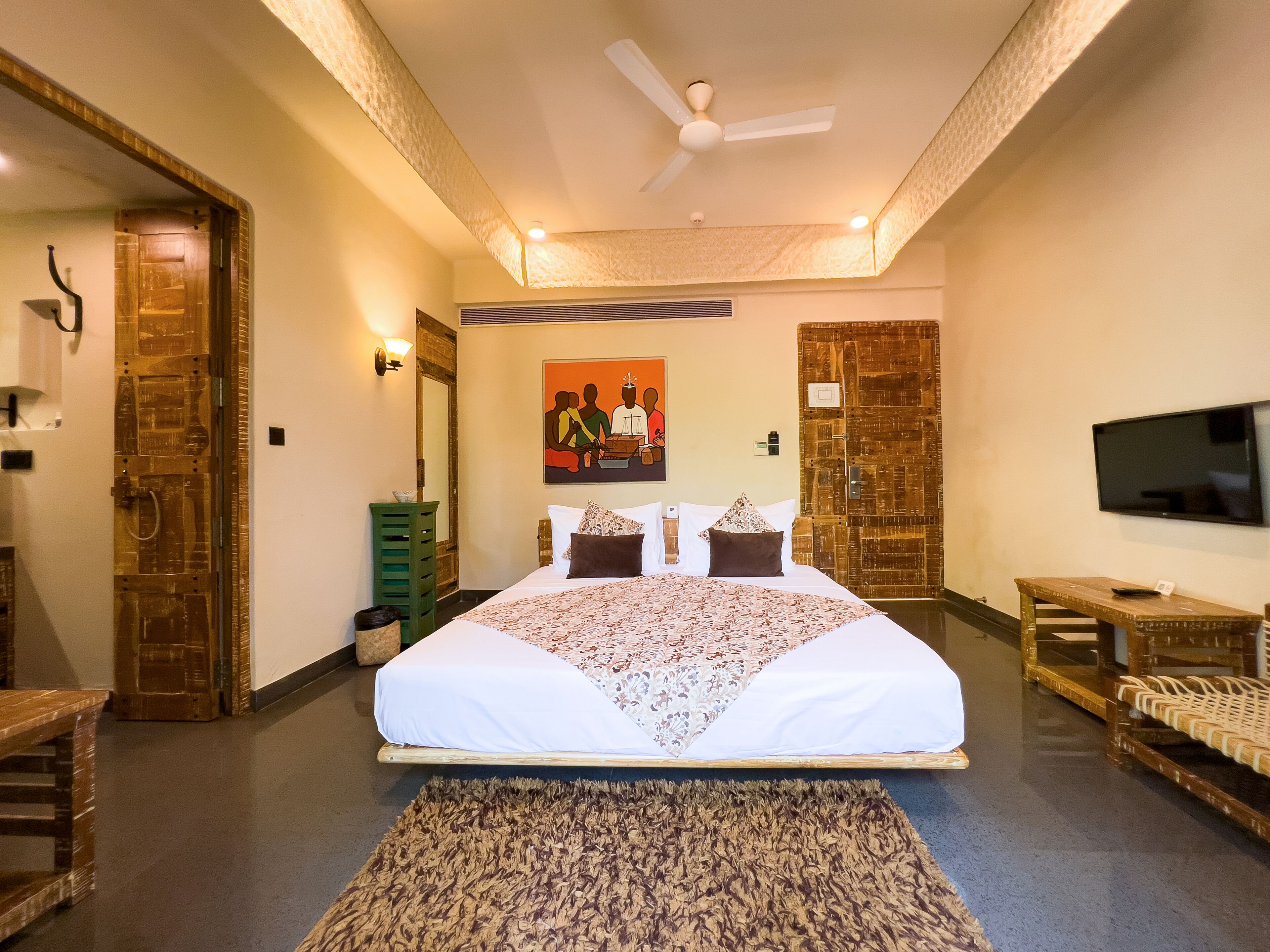 A hotel room with a large bed, a flat-screen TV, a wooden door, and a painting on the wall.