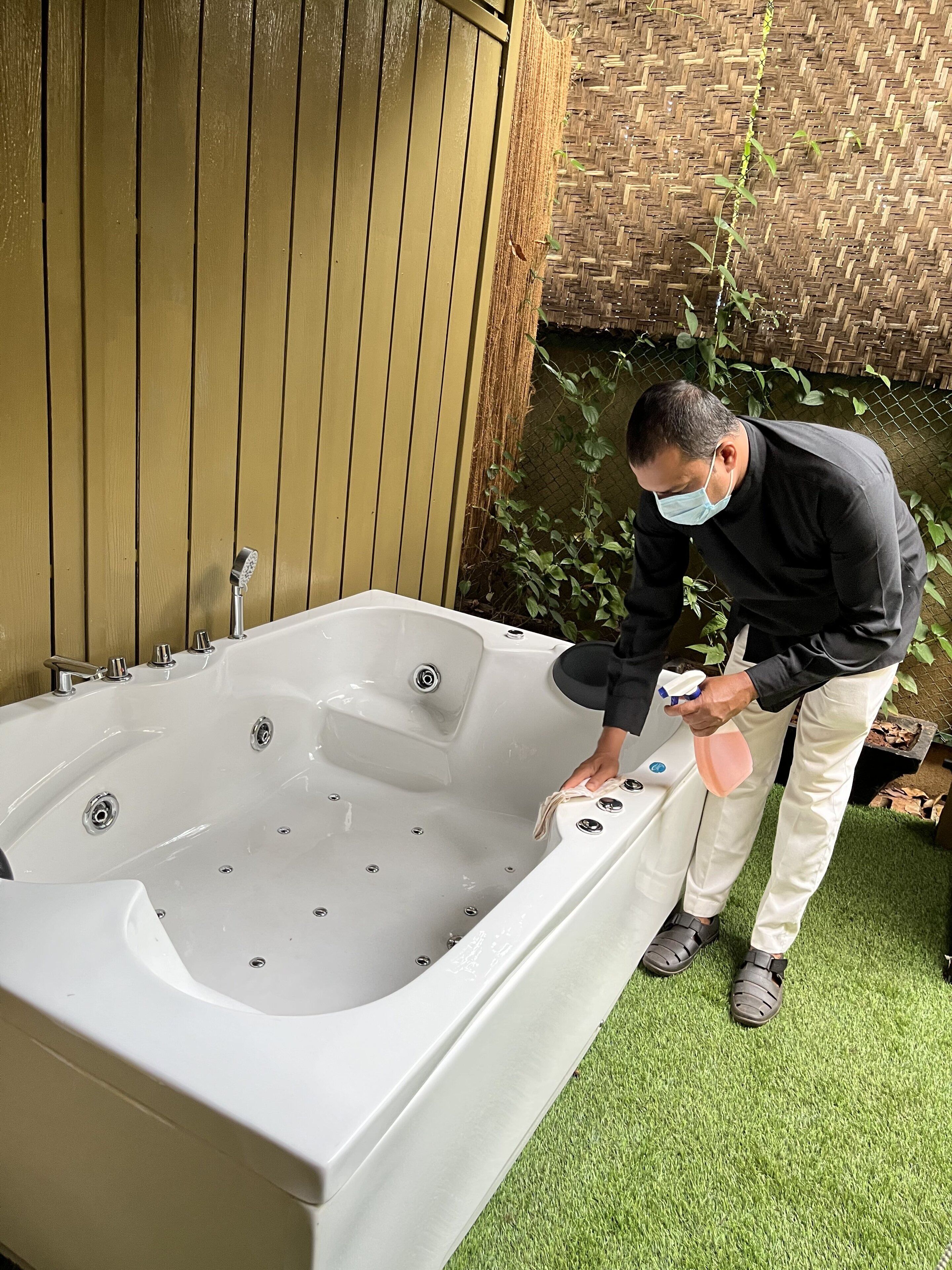 Un grand jacuzzi extérieur doté de plusieurs jets, entouré d’une clôture en bois et de verdure.