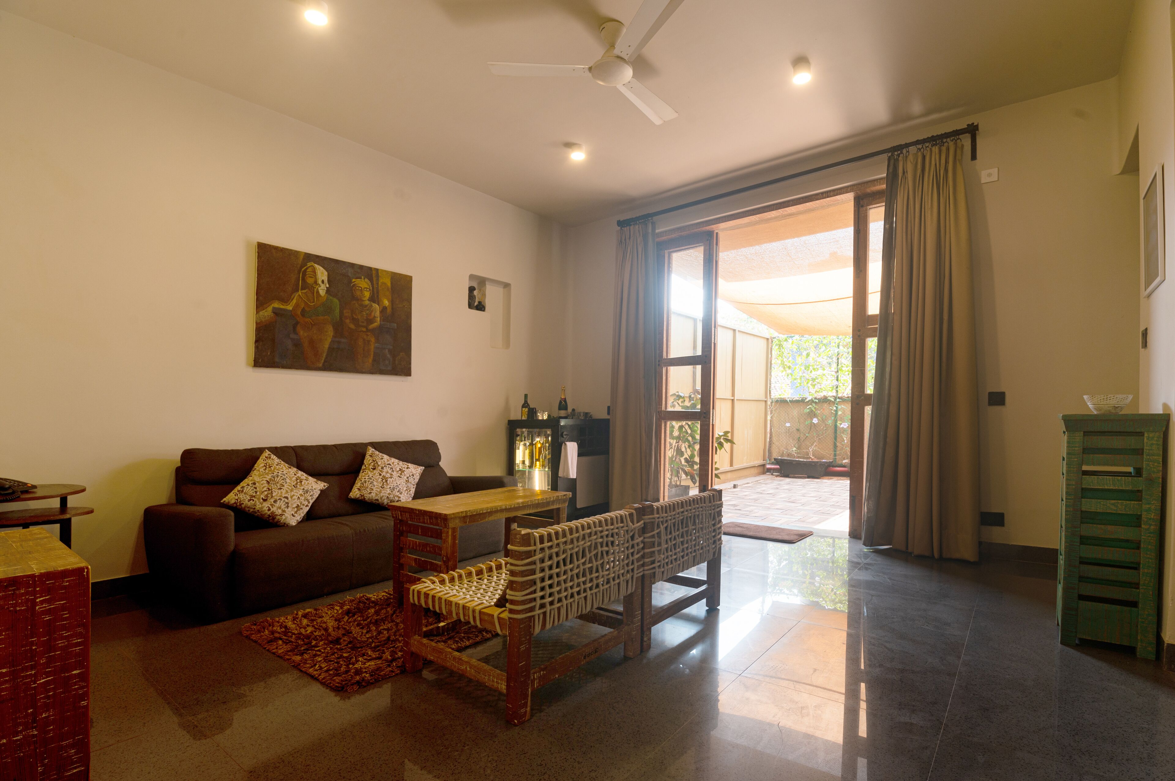A living room with a sofa, a coffee table, a wicker chair, a painting on the wall, and a sliding glass door leading to an outdoor area.