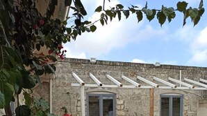 Un edificio de piedra con dos puertas de vidrio, un porche cubierto y una maceta con flores rojas.