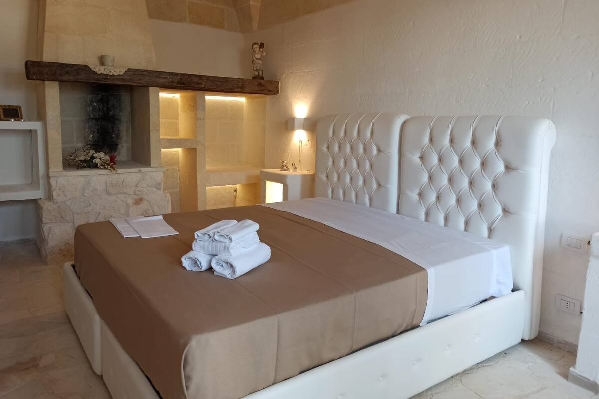 A bedroom with a large bed, stone walls, a fireplace, and a stone bench.