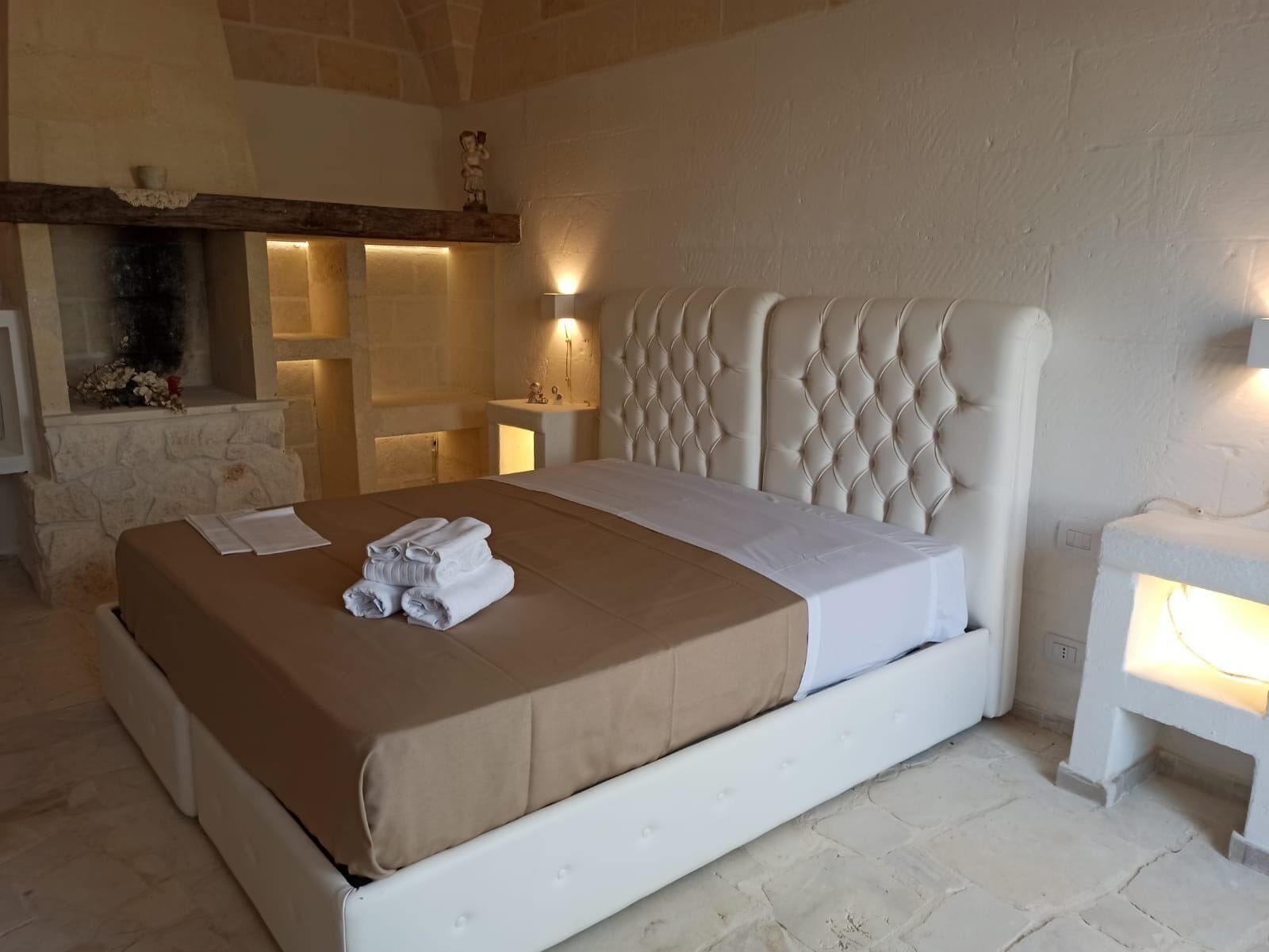 A bedroom with a white bed, a stone fireplace, and a stone wall.