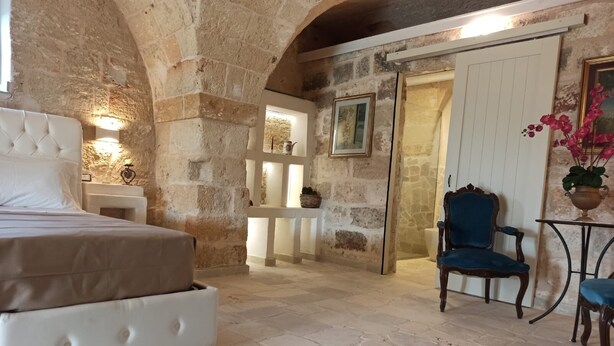 Un dormitorio con paredes de piedra, una cama, una silla y una pequeña mesa.