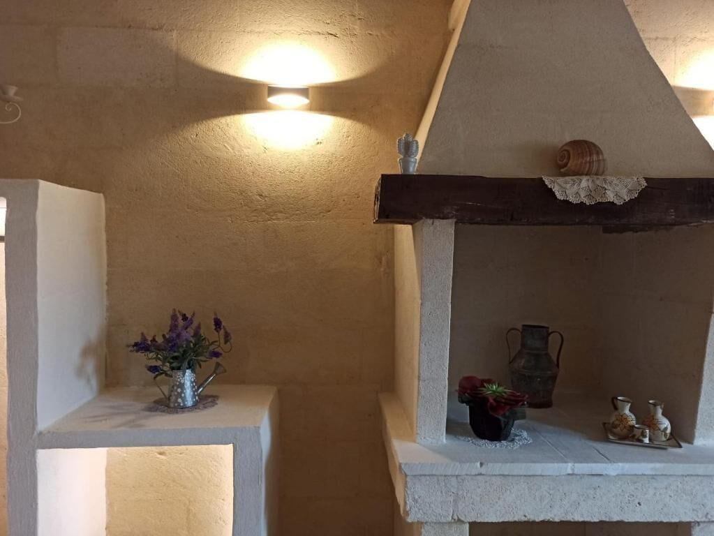 Una habitación con pared de piedra, un estante con adornos y un pequeño jarrón con flores.