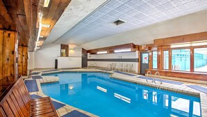 An indoor swimming pool with wooden benches and a tiled floor, surrounded by walls with a patterned ceiling and windows. - Loon Mountain Condo w/ Pool & Game Room Access! (Lincoln)
