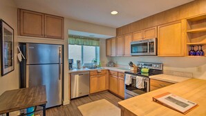 A modern kitchen with wooden cabinets, stainless steel appliances, and a window with blinds. - Loon Mountain Condo w/ Pool & Game Room Access! (Lincoln)