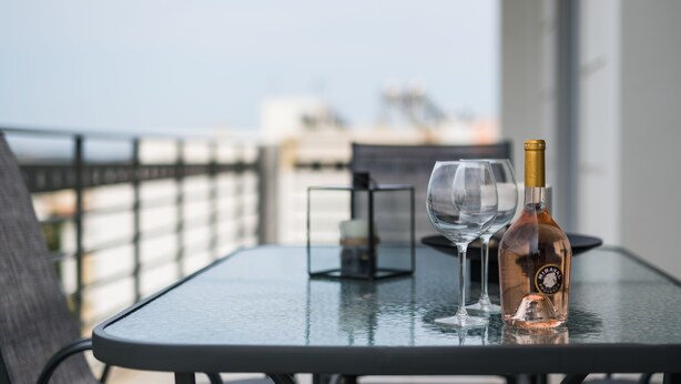 A table with a bottle and two glasses on a balcony overlooking a cityscape. - Thresh Apartments Airport by Airstay (Spata-Artemida)