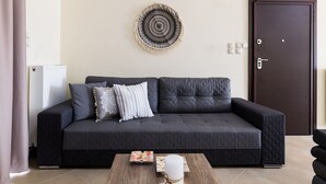 A dark grey sofa with a quilted pattern, a round wall hanging, and a wooden coffee table with a candle. - Thresh Apartments Airport by Airstay (Spata-Artemida)