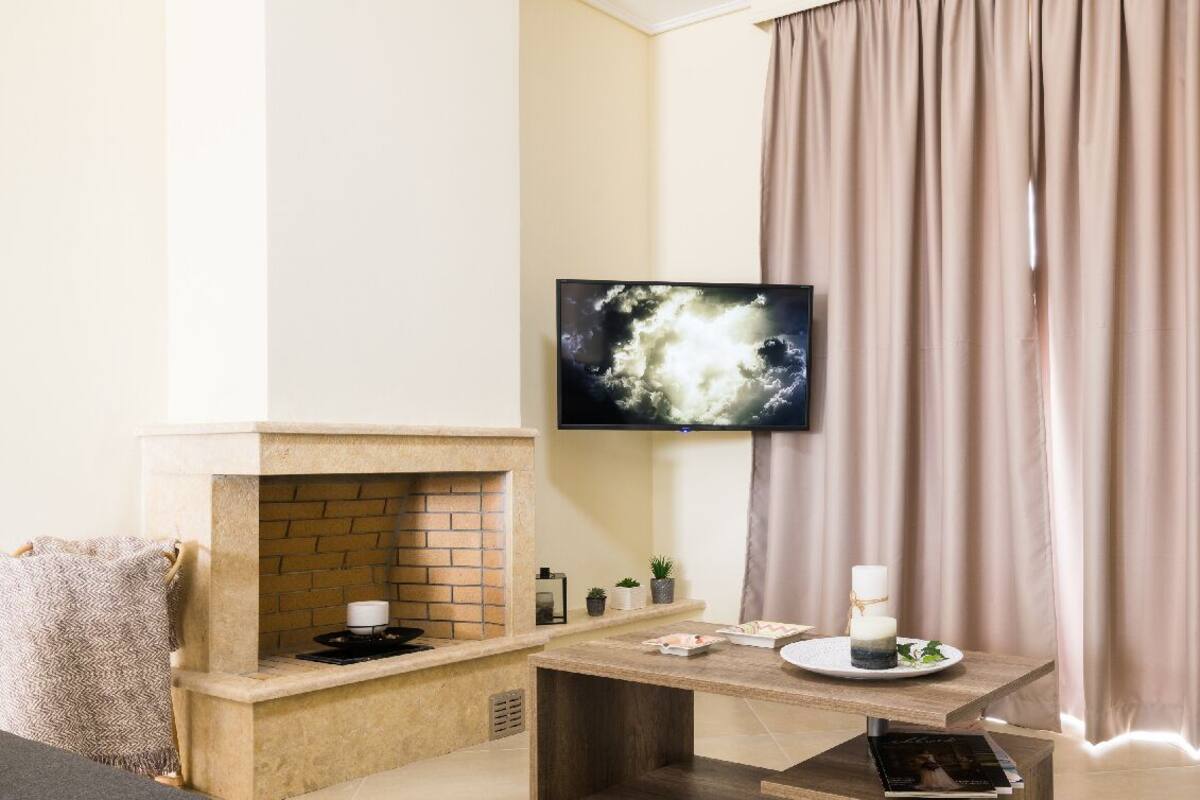 A living room with a fireplace, a flat-screen TV mounted on the wall, a table with a candle and a plate of food, and a sofa.