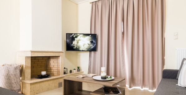A living room with a fireplace, a flat-screen TV mounted on the wall, a table with a candle and a plate of food, and a sofa. - Thresh Apartments Airport by Airstay (Spata-Artemida)