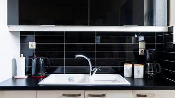 A modern kitchen with a black tiled backsplash, a white sink, and stainless steel appliances.