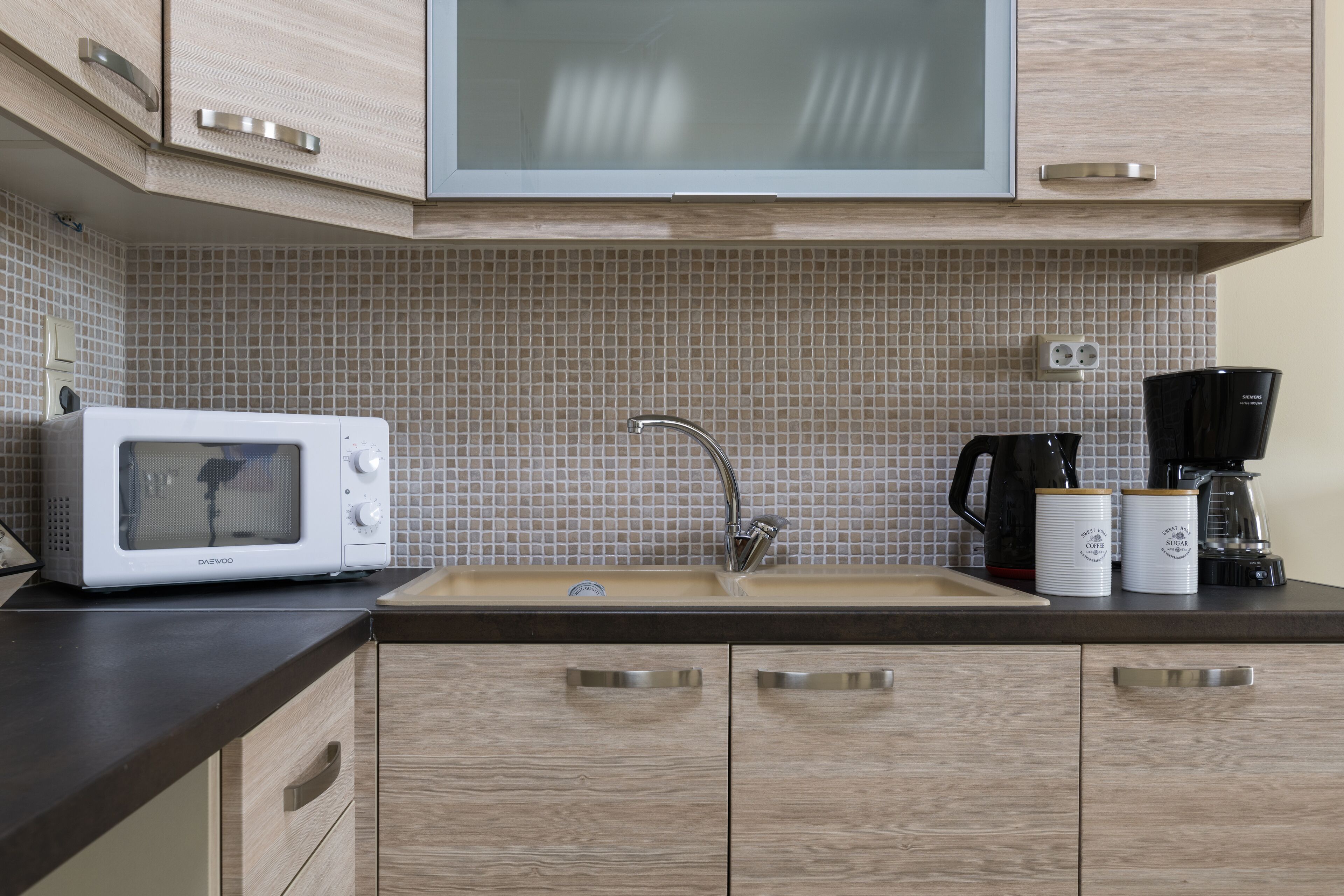 A kitchen with a microwave, sink, cabinets, and a coffee maker.